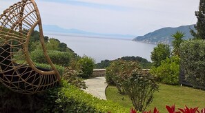 A garden with a wicker chair, a pathway, and a view of the sea. - Villa Mirothea (Alonissos)
