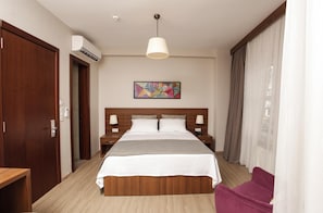 A hotel room with a wooden bed, a bedside table, a lamp, a chair, and a painting on the wall.