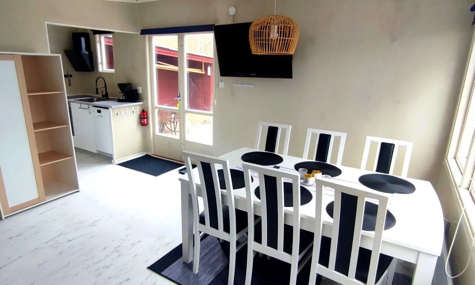 A compact kitchen with a dining area, a TV mounted on the wall, and a window providing natural light.