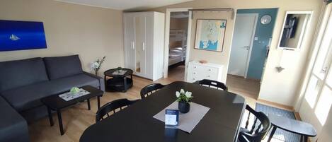 A modern living room with a sofa, coffee table, dining table, and chairs. There is a wardrobe, a bed, and a map on the wall.