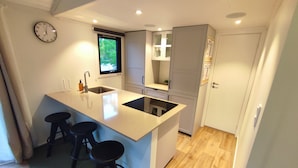 A compact kitchen with a central island, two bar stools, a built-in sink, and a clock on the wall. - Långasjönäs Camping & Stugby (Asarum)