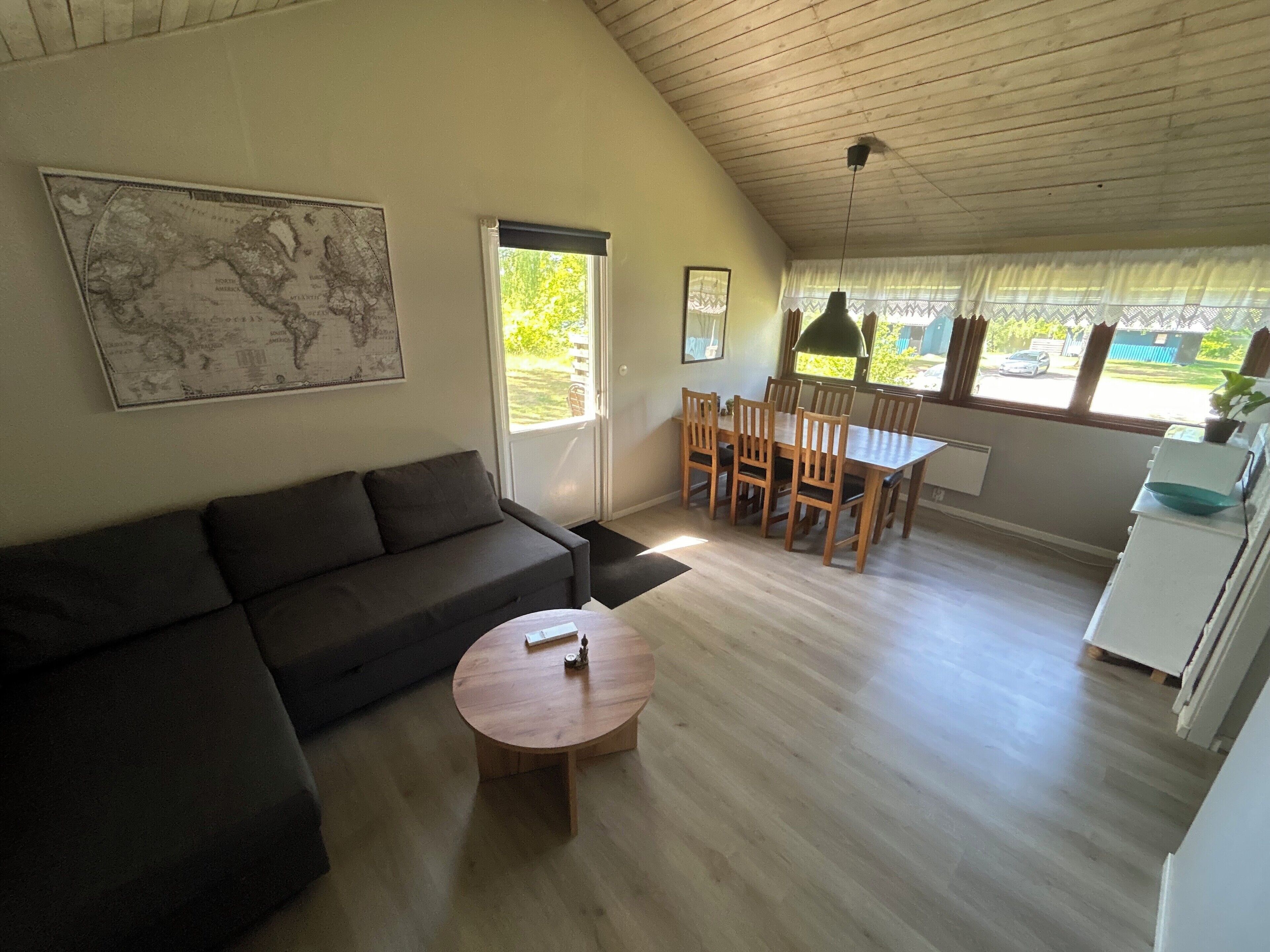 Una sala de estar con sofá, una mesa de centro redonda, una mesa de comedor con sillas, un mapa en la pared y vistas al exterior.