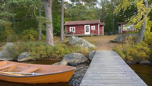 A wooden dock leading to a red cabin with a white door, surrounded by trees and rocks. - Långasjönäs Camping & Stugby (Asarum)