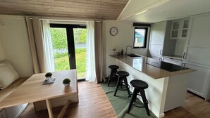 A modern kitchen with a central island, bar stools, a dining table with a plant, and a view of greenery outside. - Långasjönäs Camping & Stugby (Asarum)