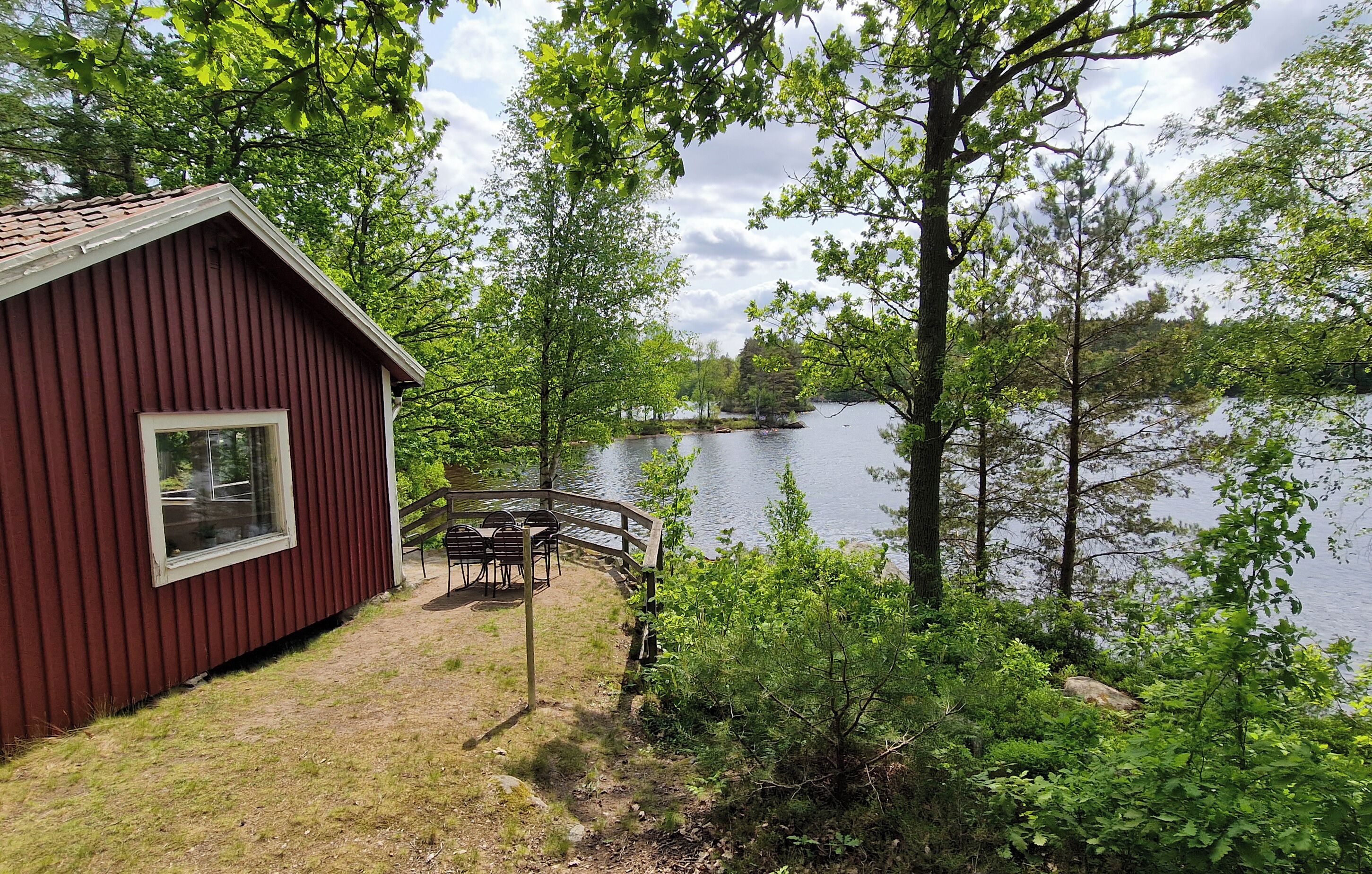 Una cabaña roja con ventana, una terraza de madera y vistas a un lago rodeado de árboles.