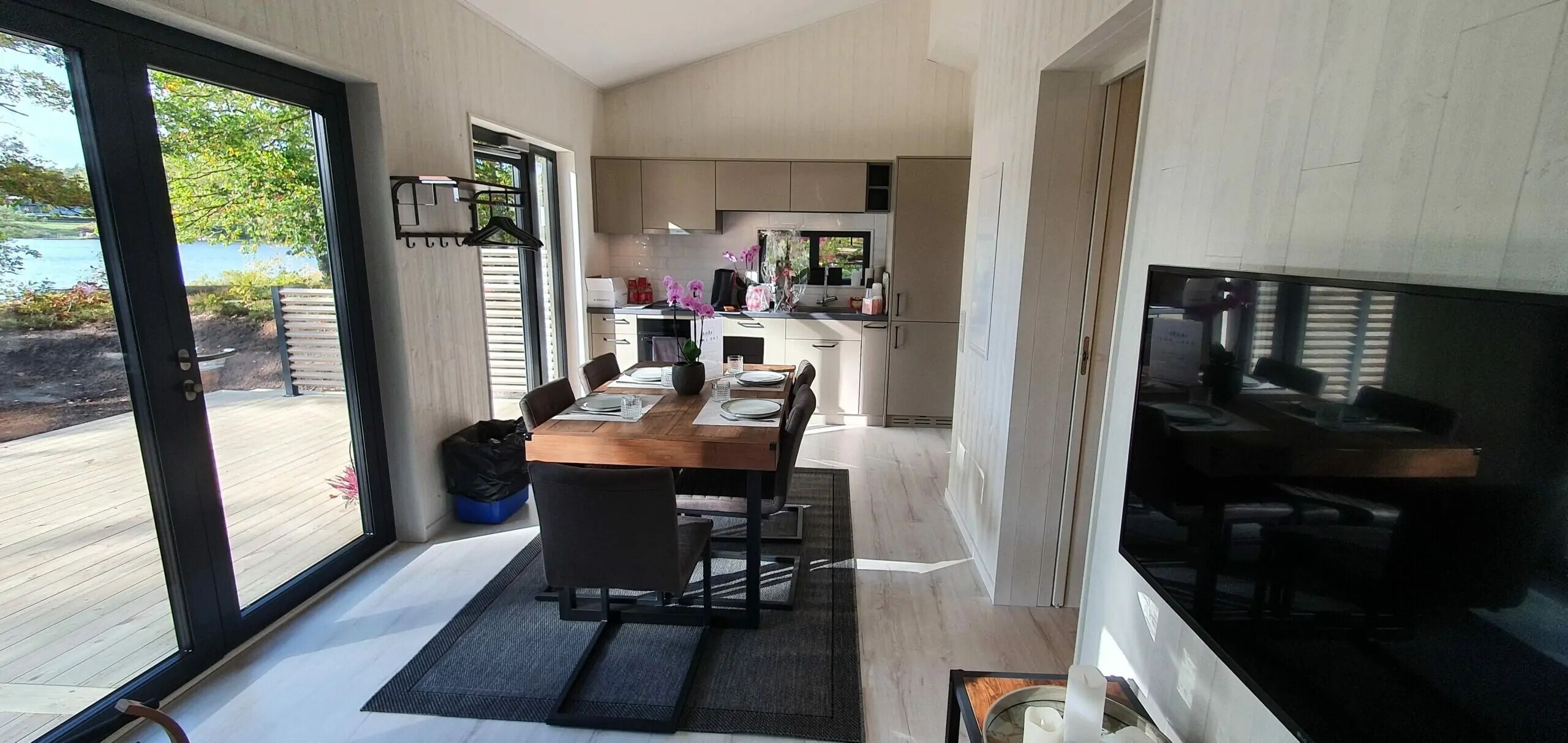 Ein modernes Interieur mit Essbereich, Küche und großen Fenstern mit Blick auf eine Terrasse.
