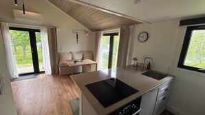 A modern kitchen with a built-in stove, a sink, and a dining area with a bench. - Långasjönäs Camping & Stugby (Asarum)