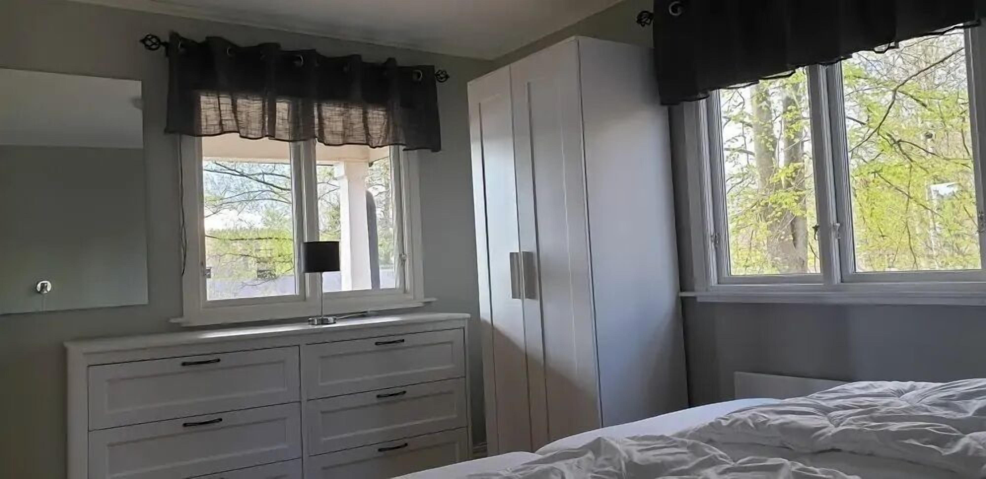 A bedroom with a bed, a dresser, a window with curtains, and a wardrobe.