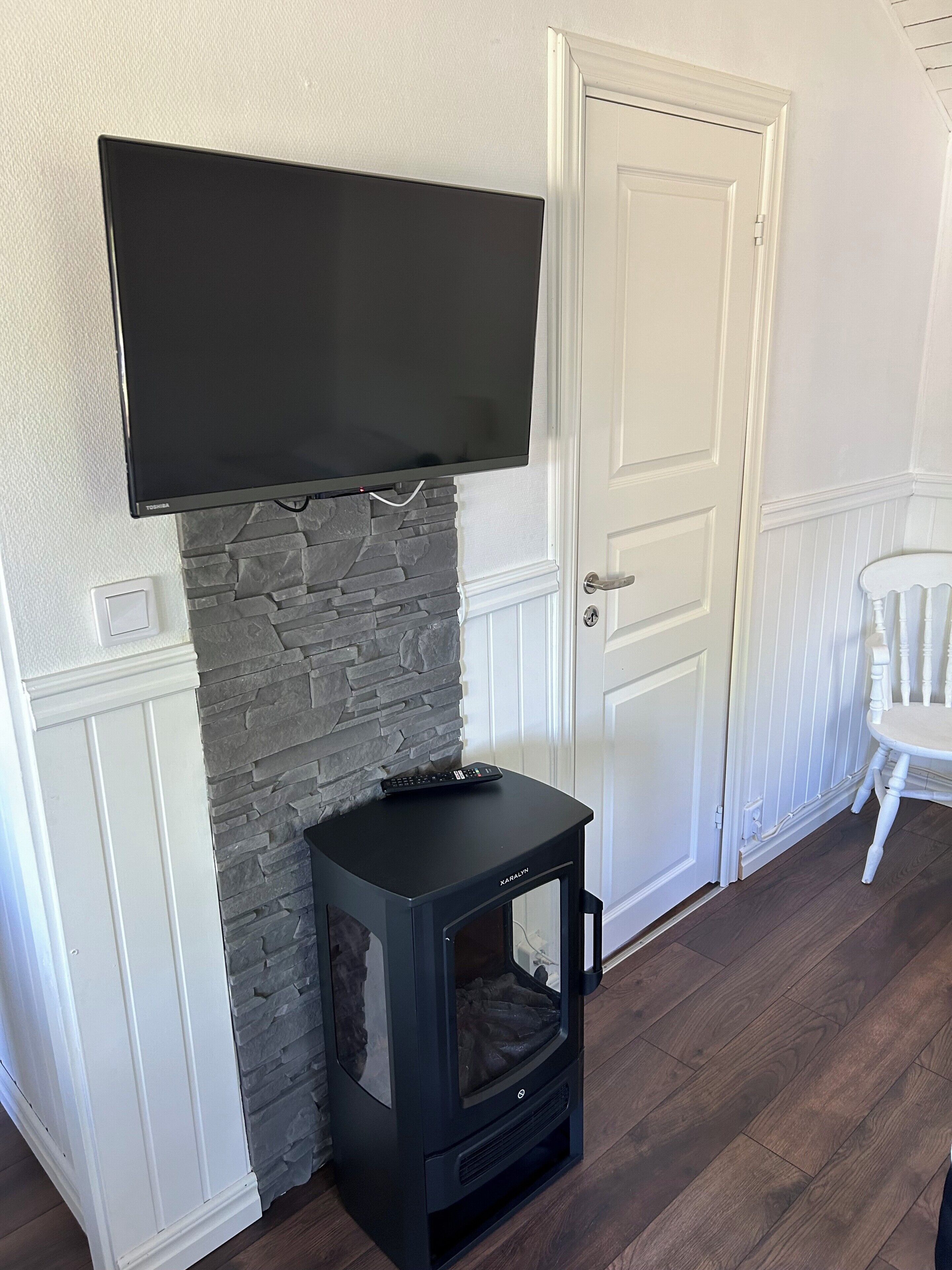 Una habitación con chimenea de piedra, estufa de madera negra, televisor de pantalla plana montado y puerta blanca.