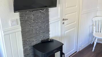 Una habitación con chimenea de piedra, estufa de madera negra, televisor de pantalla plana montado y puerta blanca.
