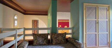 A bunk bed with patterned bedding, a window with a lattice design, and a red and yellow decorative panel.