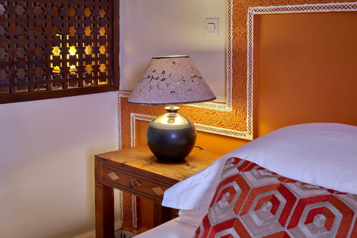Cama com almofada estampada, mesa de cabeceira com abajur e painel decorativo na parede.