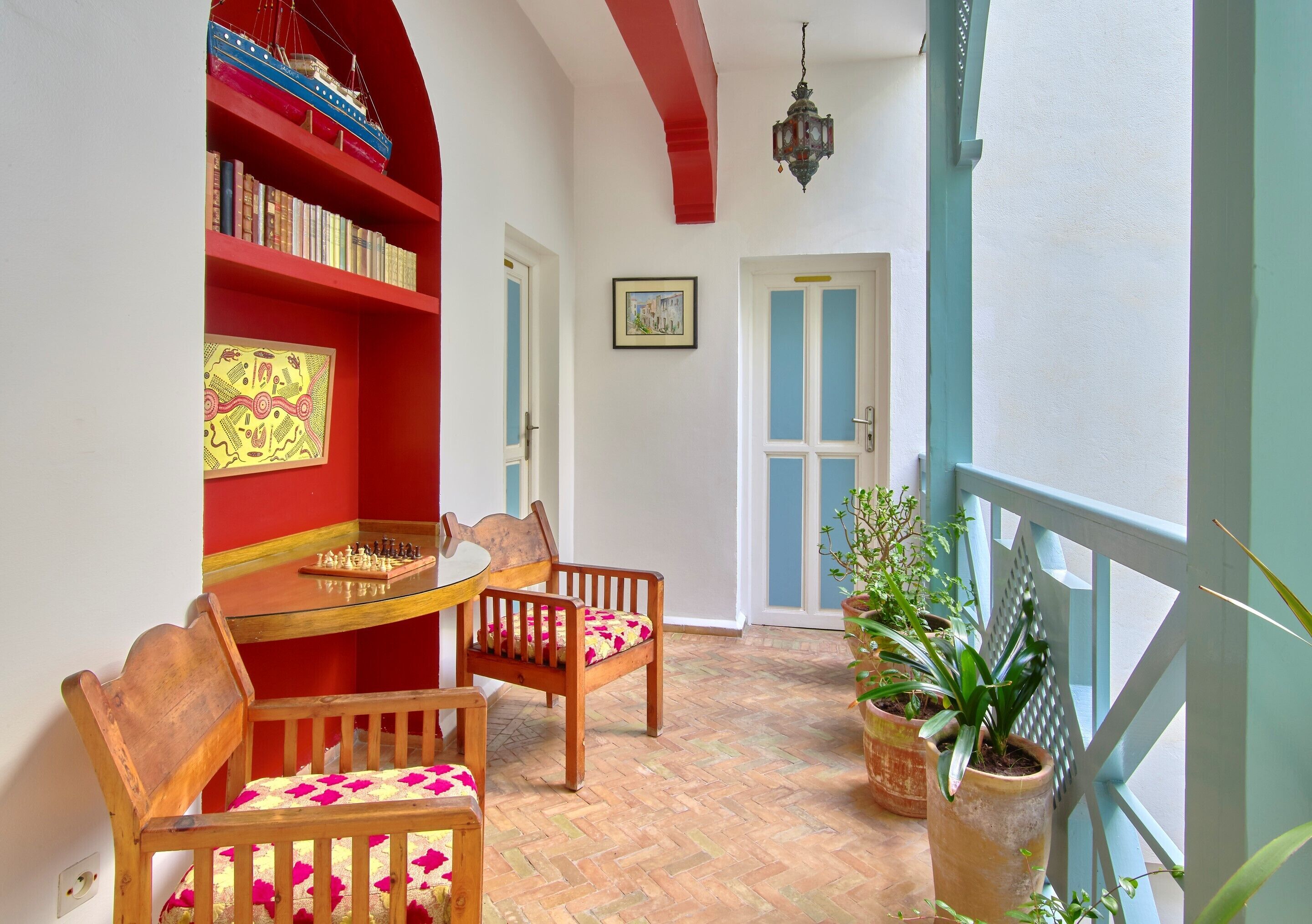 Una habitación con una mesa y sillas de madera, una estantería, una puerta y plantas en macetas.