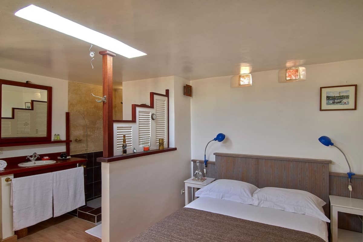 Quarto com cama, mesas de cabeceira, espelho, pia e janela com persianas.