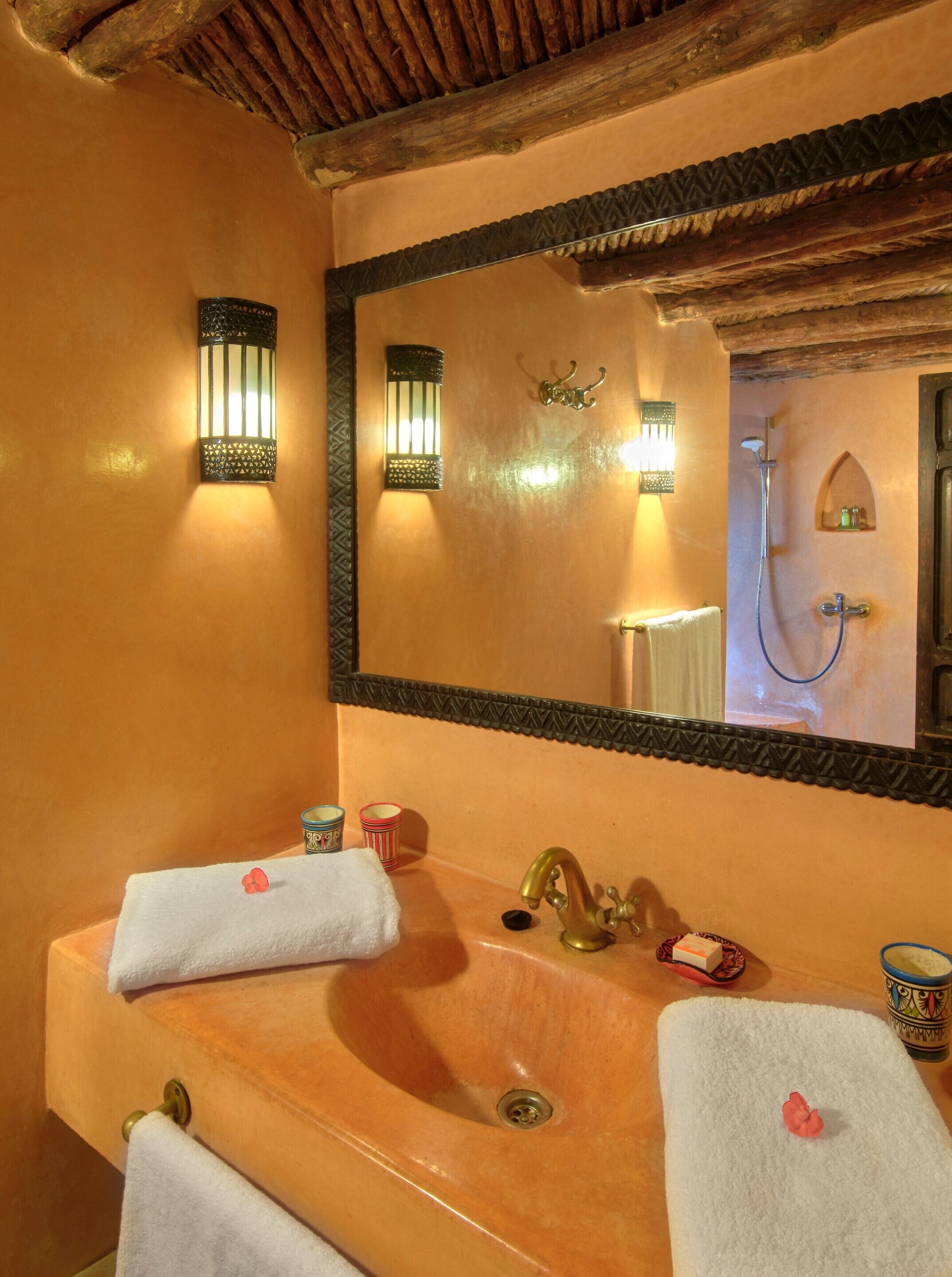 Un baño con techo de madera, un espejo grande, dos lavamanos con toallas e iluminación en la pared.