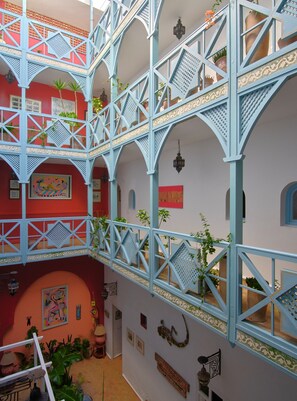 Un atrio de varios niveles con barandas azules, plantas en macetas y obras de arte en las paredes.