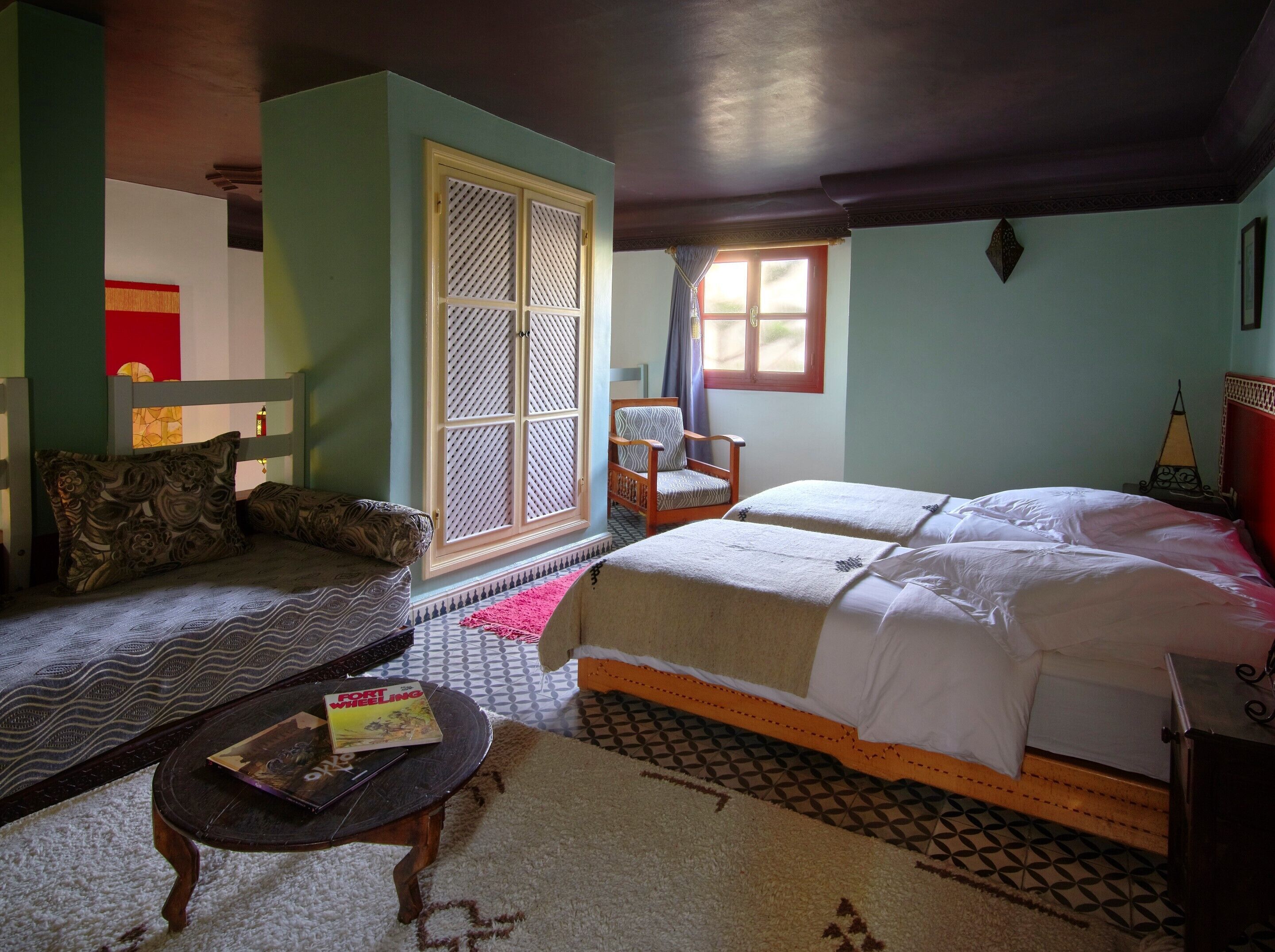 A room with a bed, two chairs, a sofa, a small table with a book, and a window with curtains.