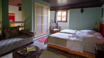 A room with a bed, two chairs, a sofa, a small table with a book, and a window with curtains.
