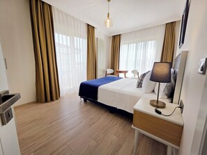 A hotel room with a bed, bedside table, lamp, and a view of the outdoors through large windows. - Kamer Exclusive Hotel & Suites (Cesme)