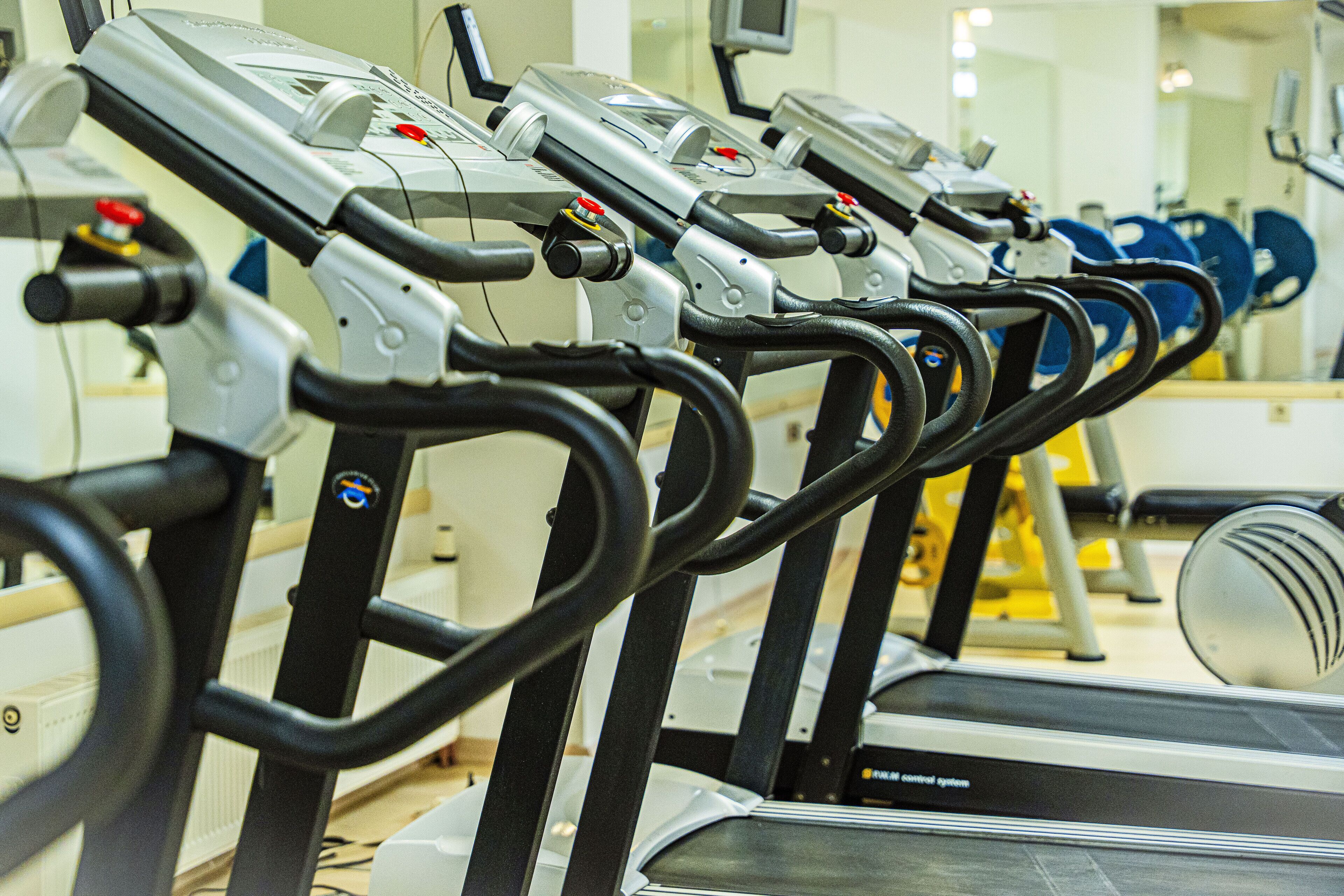 Varias bicicletas estáticas en un gimnasio con un espejo en la pared y equipo de ejercicio al fondo.