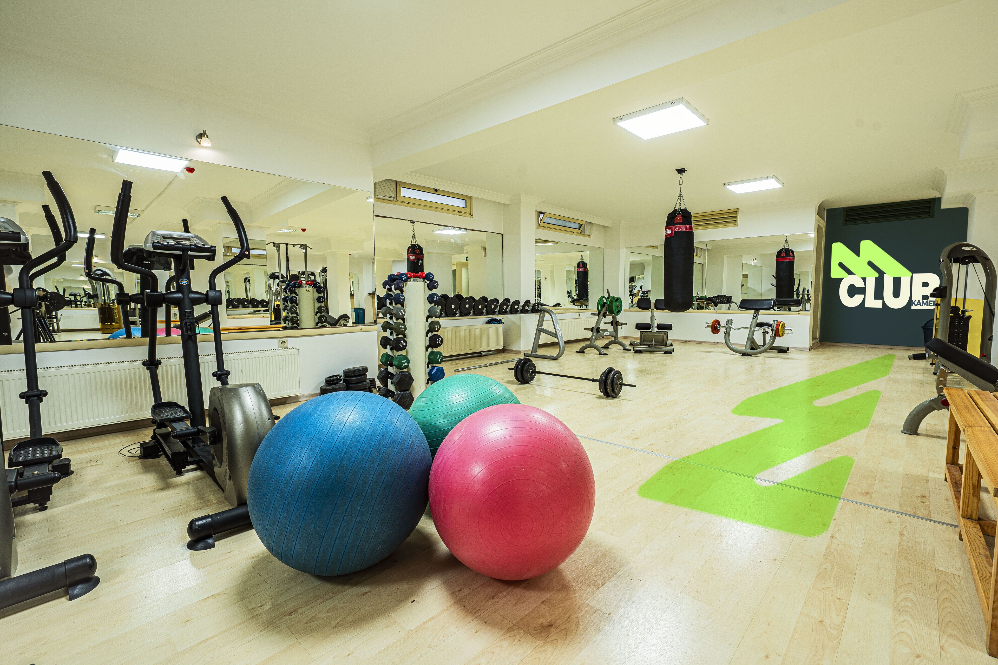 A gym with exercise equipment, large exercise balls, and a green directional arrow on the floor.