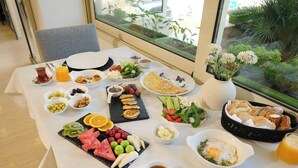 A breakfast table with various dishes, a vase with flowers, and a view of greenery outside. - Kamer Exclusive Hotel & Suites (Cesme)