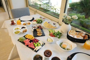A breakfast table with various dishes, a vase with flowers, and a view of greenery outside. - Kamer Exclusive Hotel & Suites (Cesme)