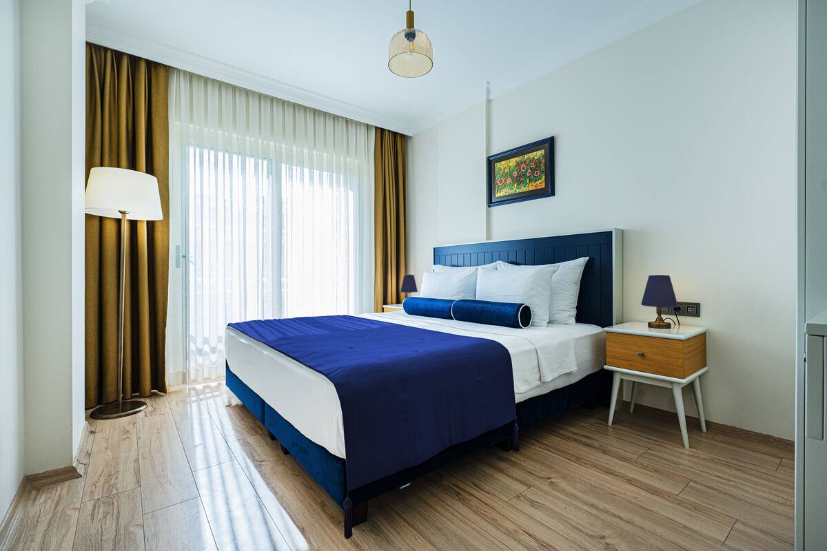 A hotel room with a bed, bedside table, lamp, and artwork on the wall.