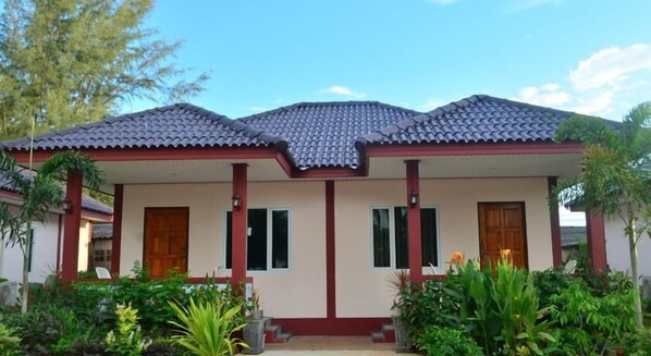A two-story house with a tiled roof, a central entrance, and a garden with various plants.