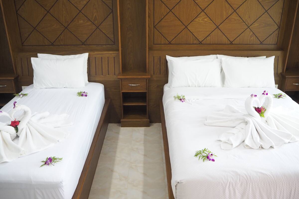Two neatly made beds with white linens and floral decorations, wooden headboards with a diamond pattern, and a small wooden nightstand between them.