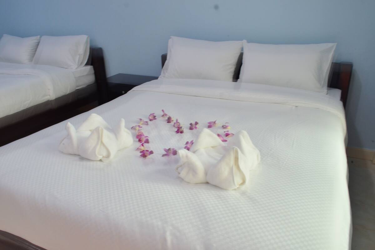 A neatly made bed with white linens and a heart-shaped arrangement of towels and flowers on the bed.