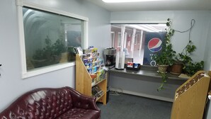 Una habitació amb un sofà de pell, una prestatgeria amb revistes, una màquina de cafè i un logotip de Pepsi a la paret.