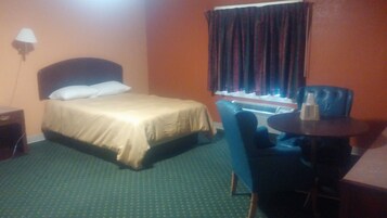 Habitación de hotel con cama, una silla, una mesita y una ventana con cortinas.