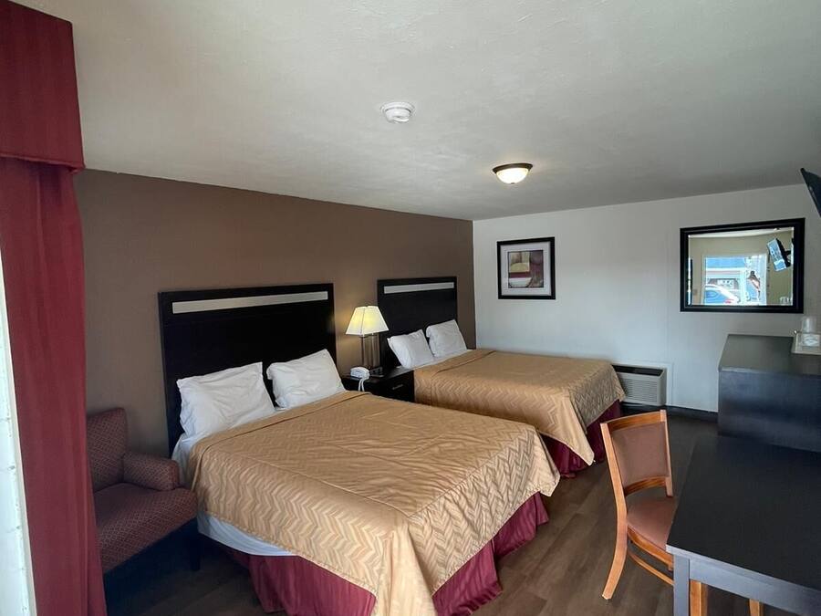 A hotel room with two beds, a desk, a chair, and a television.