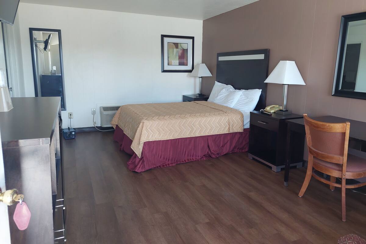 A hotel room with a bed, bedside tables, a chair, a desk, and a mirror.