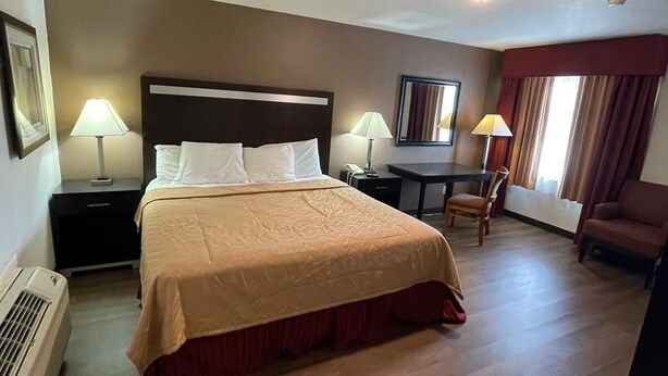 Habitació d'hotel amb un llit gran, dues taules de nit amb làmpades, un escriptori amb una cadira i una finestra amb cortines.