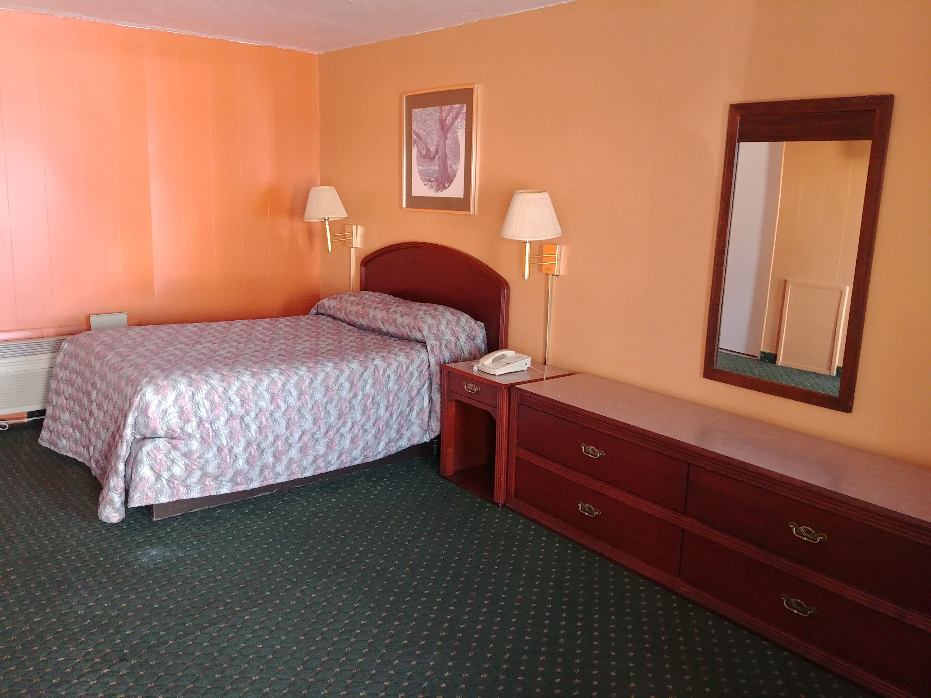 A hotel room with a bed, bedside lamps, a telephone, a dresser, and a mirror.