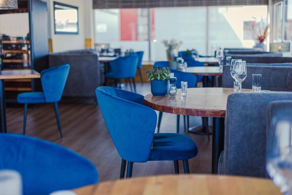 A restaurant interior with blue chairs, round tables, and a potted plant on the table.
