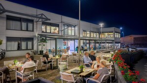 Un café en plein air avec des tables et des chaises, un bâtiment en arrière-plan et un lampadaire.