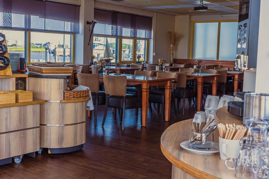 En restaurant med flere borde og stole, en disk med kasseapparat og store vinduer med udsigt ud til det fri.