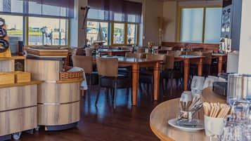 En restaurant med flere borde og stole, en disk med kasseapparat og store vinduer med udsigt ud til det fri.