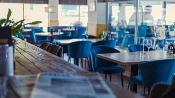 Interior de restaurante con mesas, sillas, una barra de madera y vistas a través del ventanal.