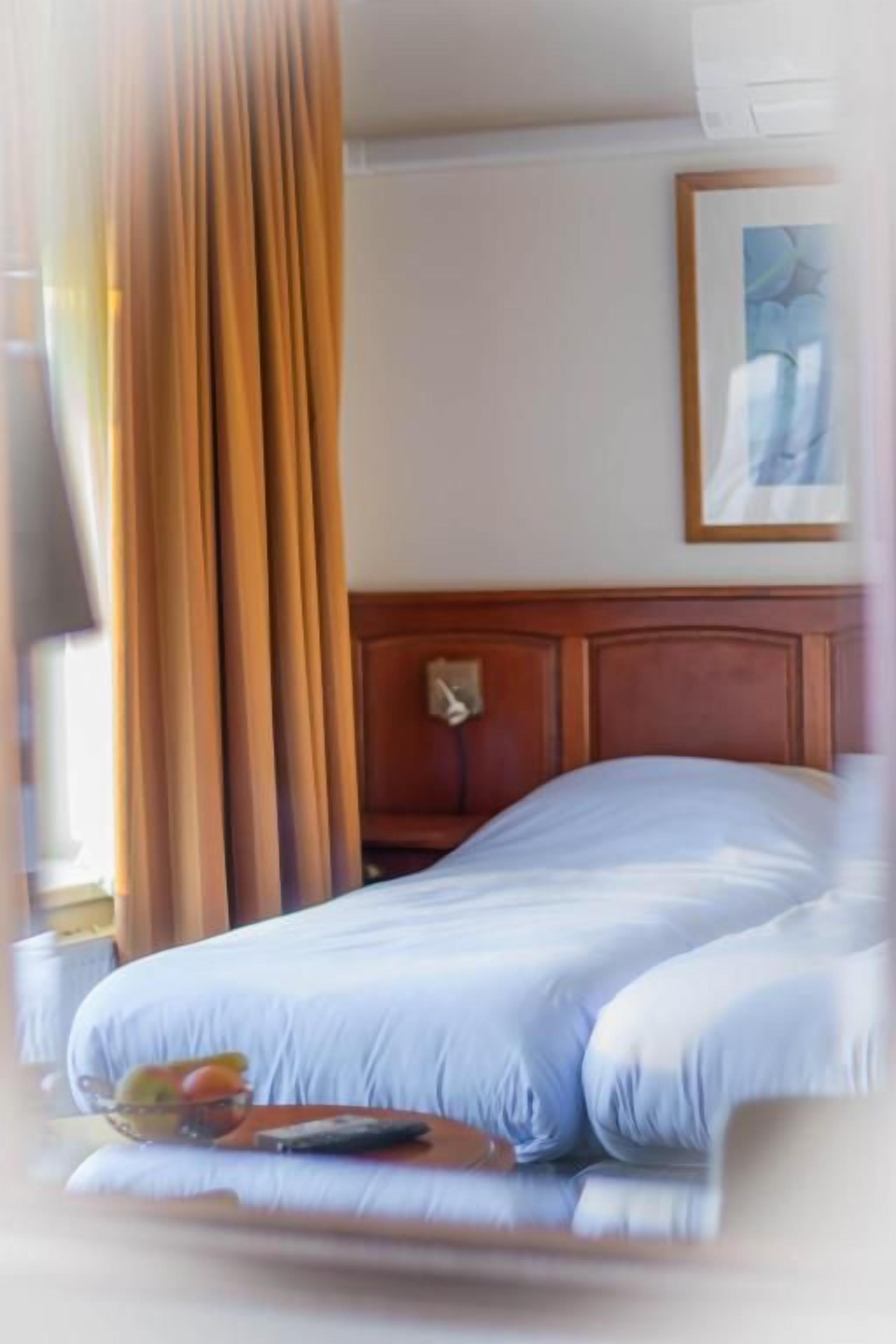 Ein Hotelzimmer mit einem Bett, Vorhängen, einem Bild an der Wand und einem kleinen Tisch mit einer Schale und einer Fernbedienung.