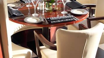 A dining area with a round table set for two, complete with plates, cutlery, and wine glasses.