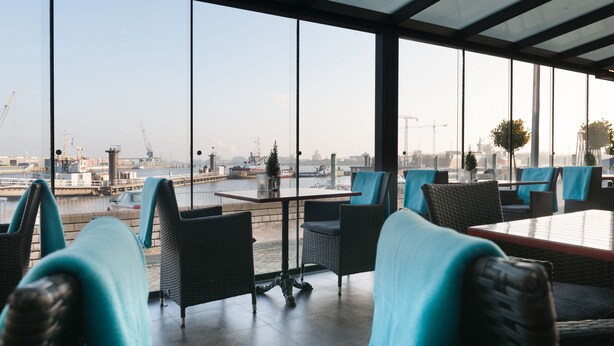 Un espace de détente intérieur moderne, avec vue sur un port, comprenant des meubles en osier et une cloison en verre.