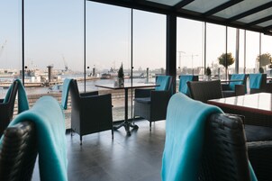 Uma área de estar interna moderna com vista para um porto, com móveis de vime e um painel de vidro.