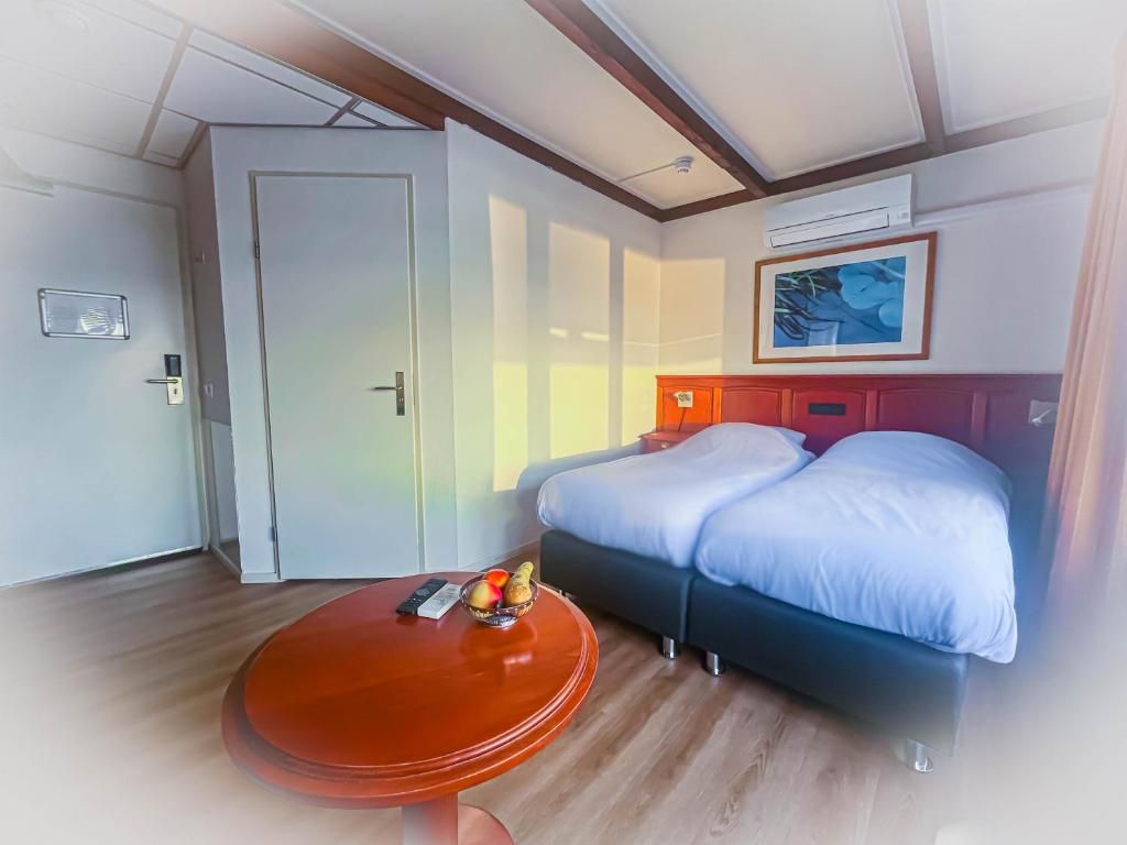 A hotel room with a bed, a round table with a fruit bowl, a door, and a framed picture on the wall.