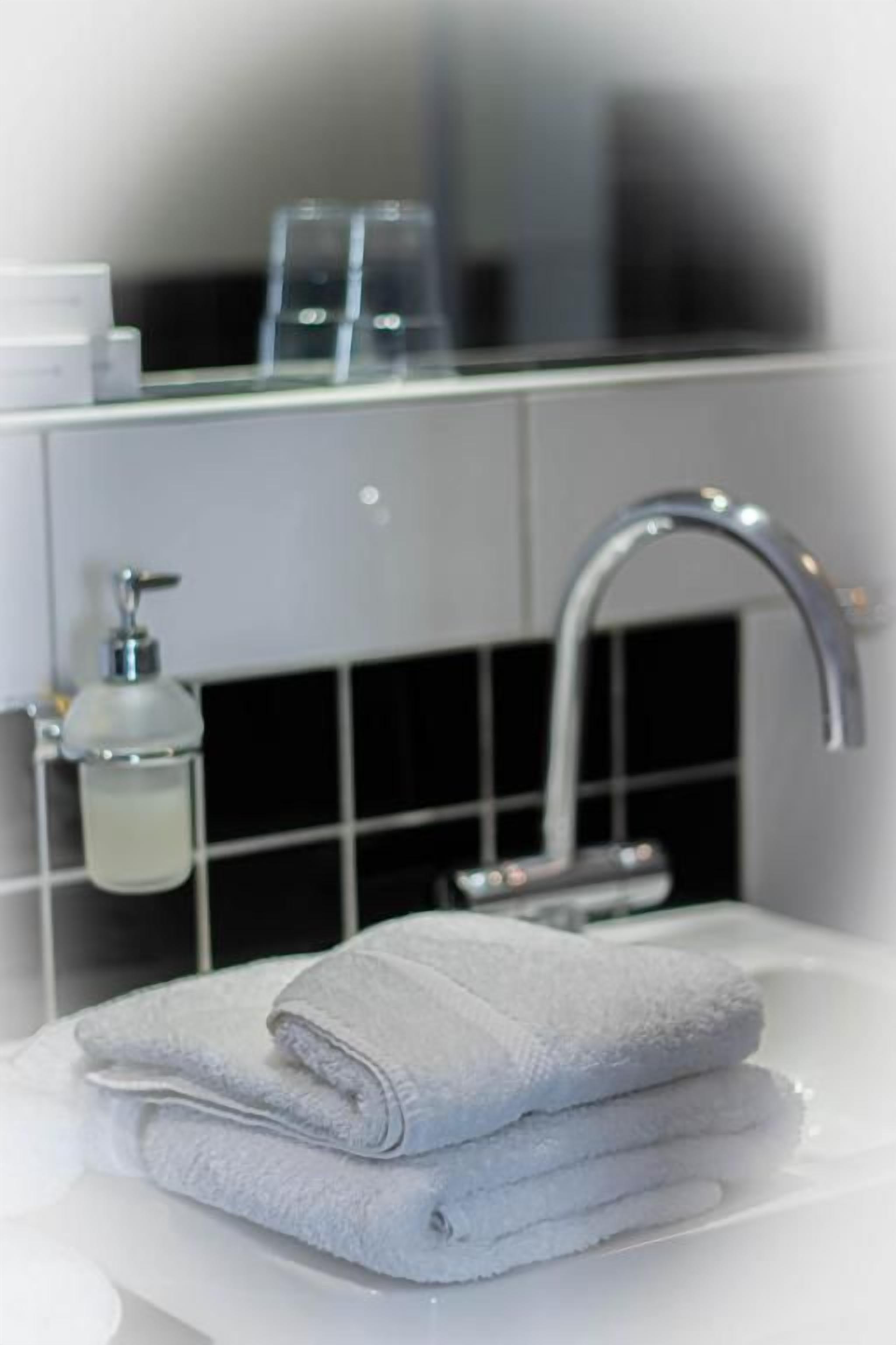 Een badkamer met een wit wastafel, een handdoek, een spiegel en een zeepdispenser.