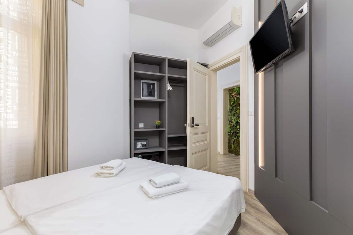 A modern hotel room with a neatly made bed, a built-in wardrobe, and a flat-screen TV mounted on the wall.