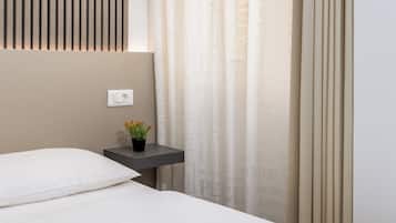A neatly made bed with white linens, a bedside table with a small plant, and a black pendant light.